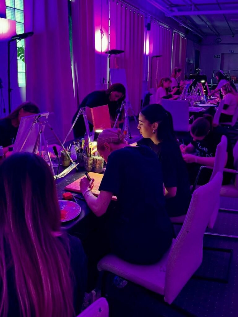 Teilnehmende malen gemeinsam beim Neon Painting Workshop unter Schwarzlicht im Femme ART Atelier in Mannheim.